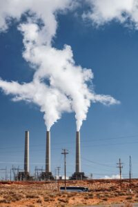De hautes cheminées dans une usine industrielle avec de la fumée contre un ciel bleu.